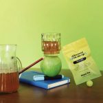 Afternoon Pick-Me-Up Tea with glass cup, pitcher, green apple, and notebook on a green backdrop.