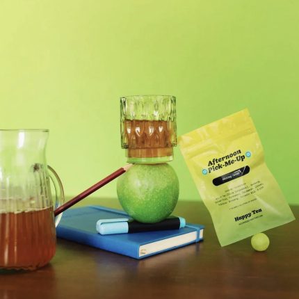 Afternoon Pick-Me-Up Tea with glass cup, pitcher, green apple, and notebook on a green backdrop.