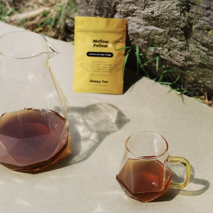 Pitcher and cup of Mellow Fellow Tea outdoors with yellow tea pouch in the background.